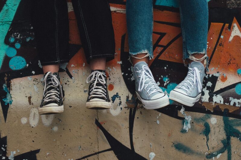 Two teenagers sit with their legs dangling over a wall.