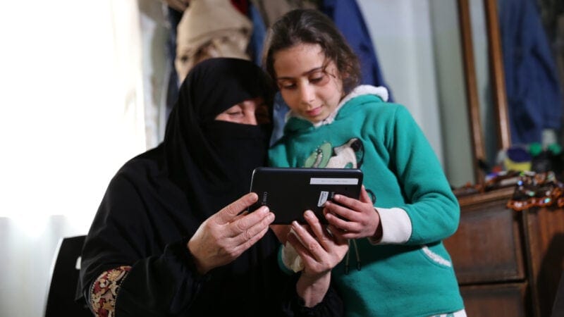 A caregiver and a child play a game on the phone together.