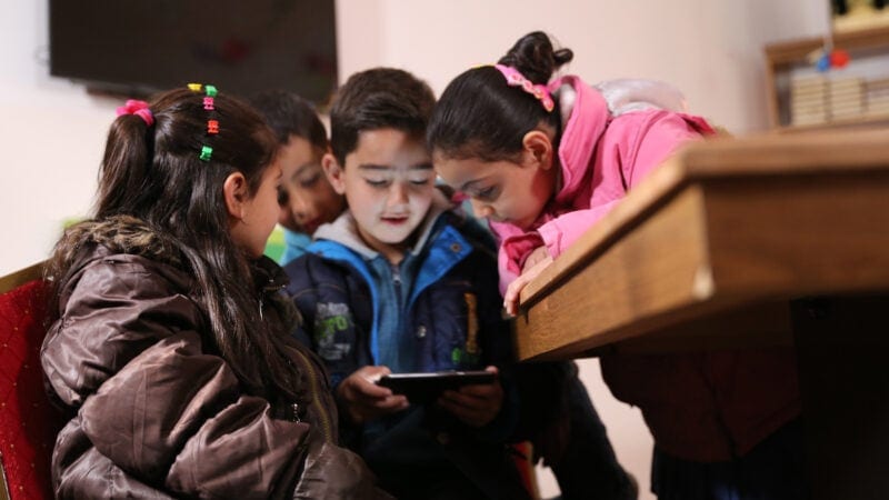 Children attentively look at a tablet together.