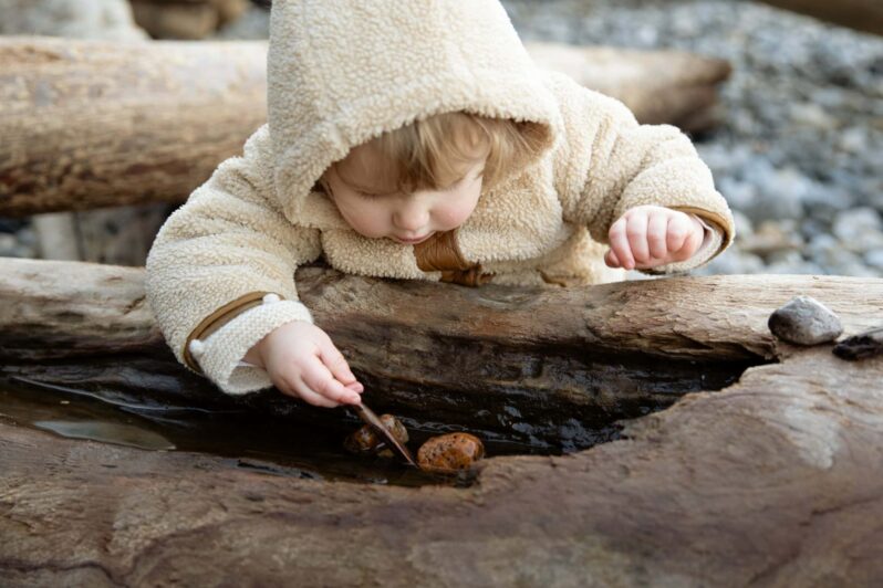 A young child plays with stones on a log.
