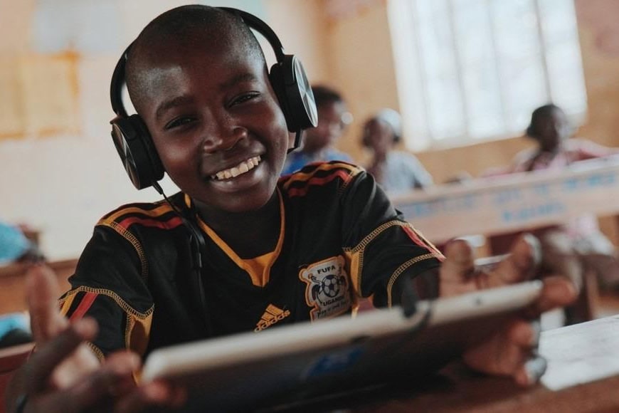 A child holding a tablet in a classroom in Uganda.