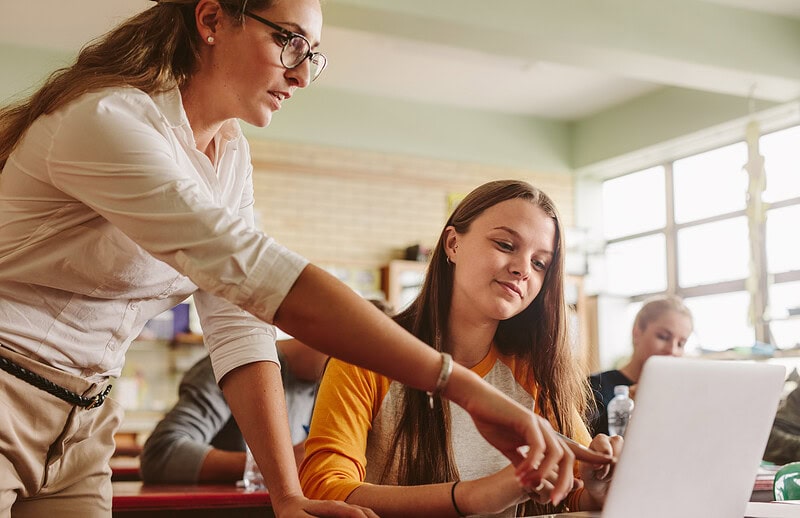 A teacher helps a student with school work on a laptop.