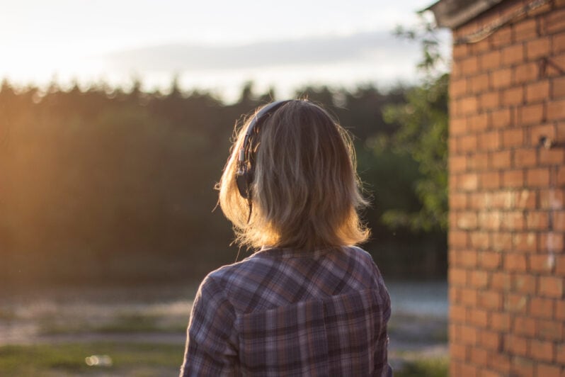 A teenager wearing headphones looks out at nature.