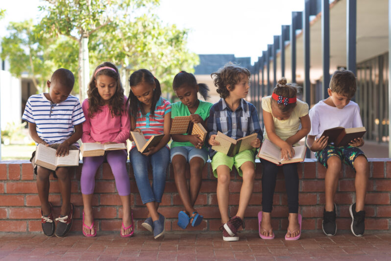 Children sit on a wall reading.