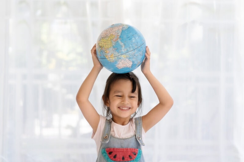 A smiling child holds a globe over her head.