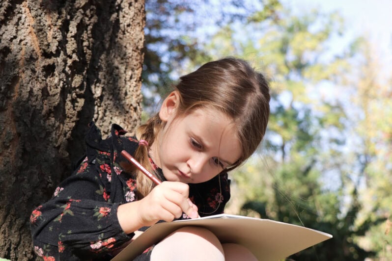 A child sits next to a tree drawing.