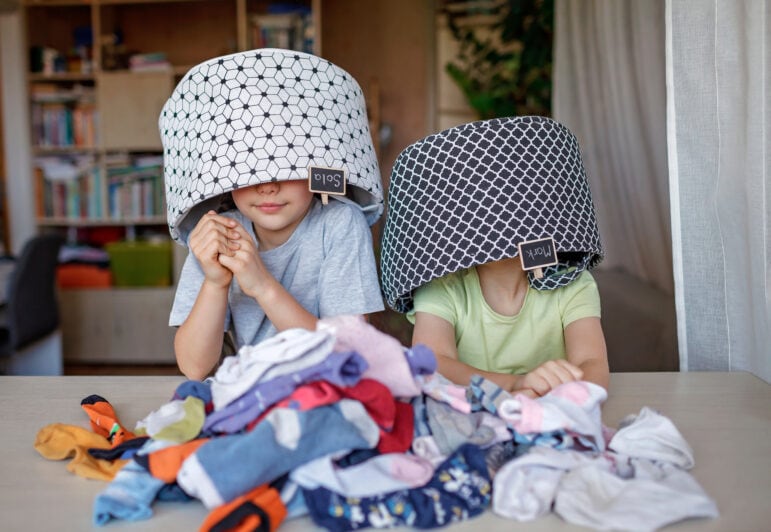 Two children helping with the washing. They are playing with washing baskets over their heads and a pile of clean socks in front of them.