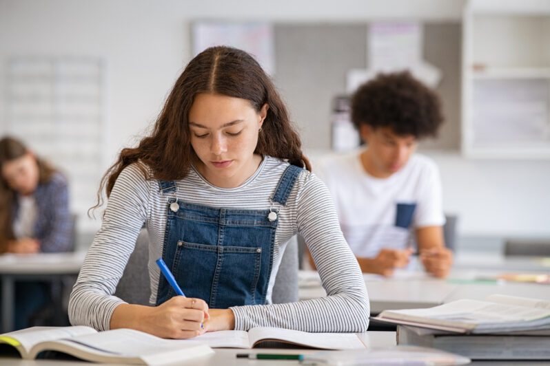 High school student taking notes from book for her study.
