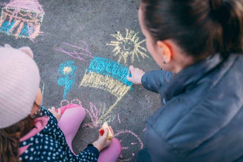 A child and parent draw a Ukrainian flag in chalk on the ground.