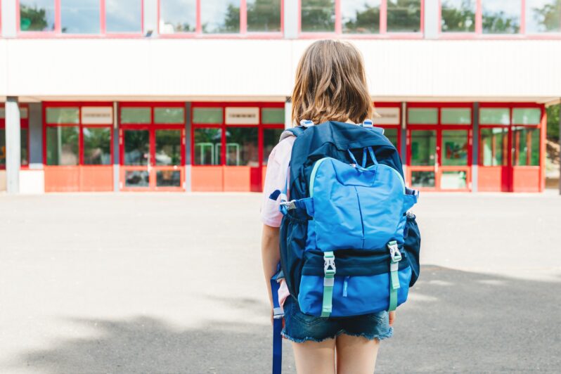 A child wearing a backpack looks at a school.