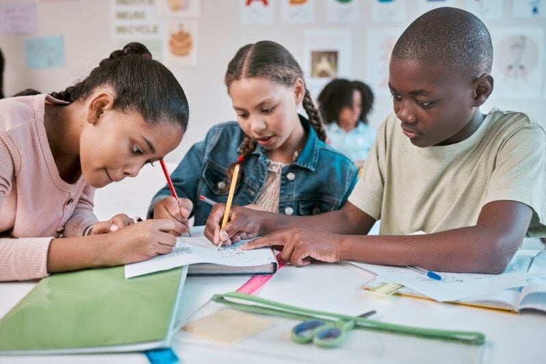 Children write on worksheets together in a classroom.