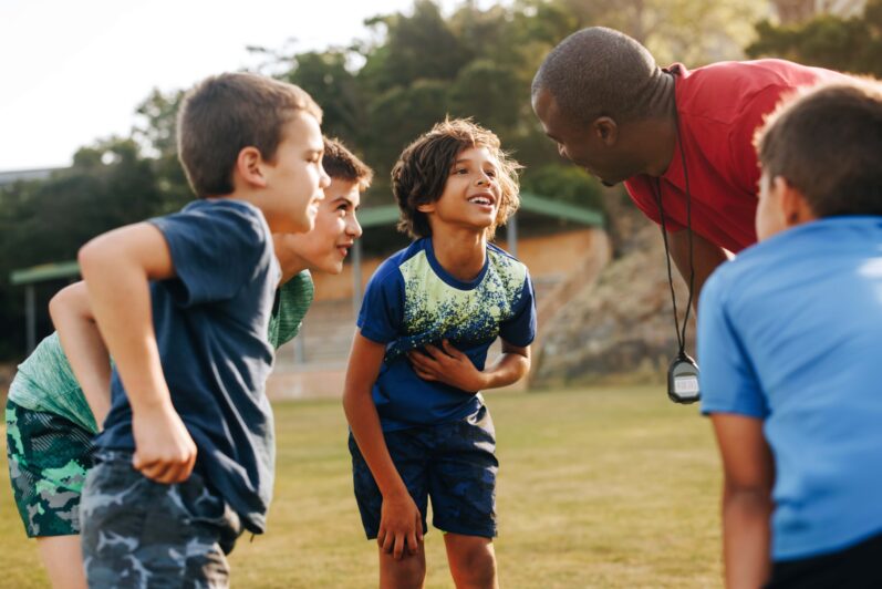 A sports teacher speaks with a small group of students outdoors.