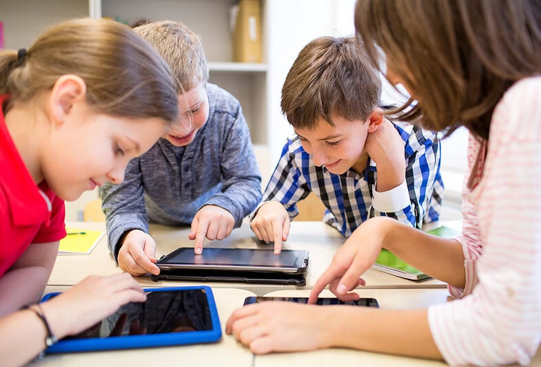 Children gathered around a desk using tablets