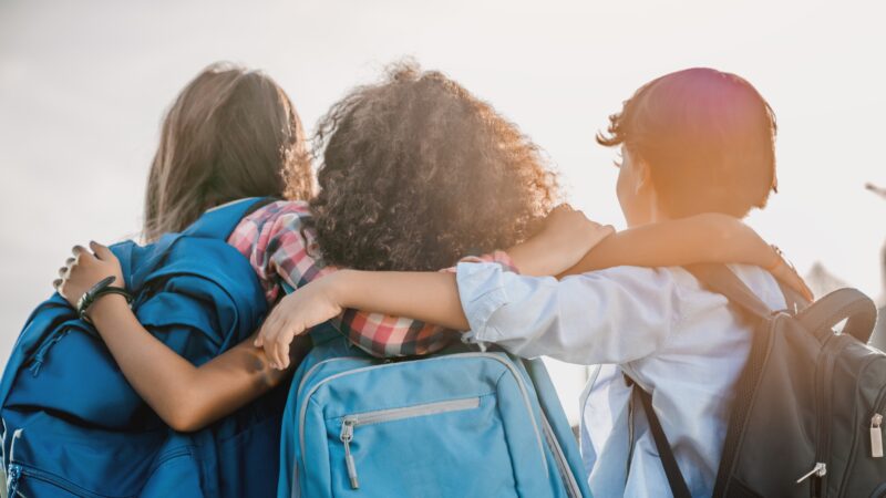 Three children stand with their arms around each others' shoulders.