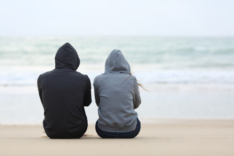 Two young people sit side by side looking out at the sea.