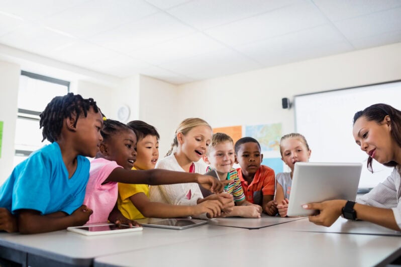 An educator teaches a group of students with a tablet.