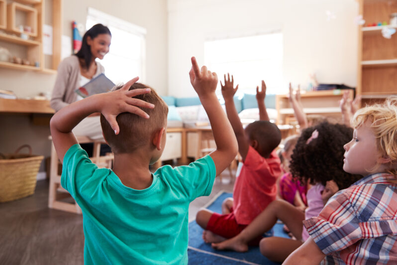 Children in a classroom raise their hands to answer a teacher's question.