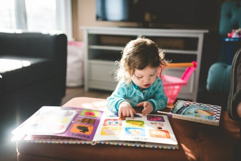 A toddler reads a picture book at home.